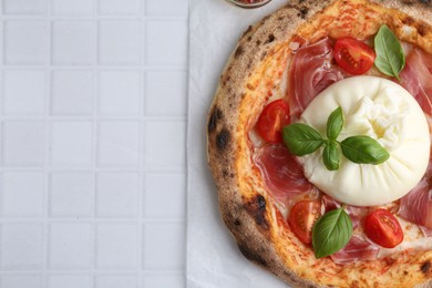 Photo of Delicious pizza with burrata cheese, basil, tomato and ham on white tiled table, top view. Space for text