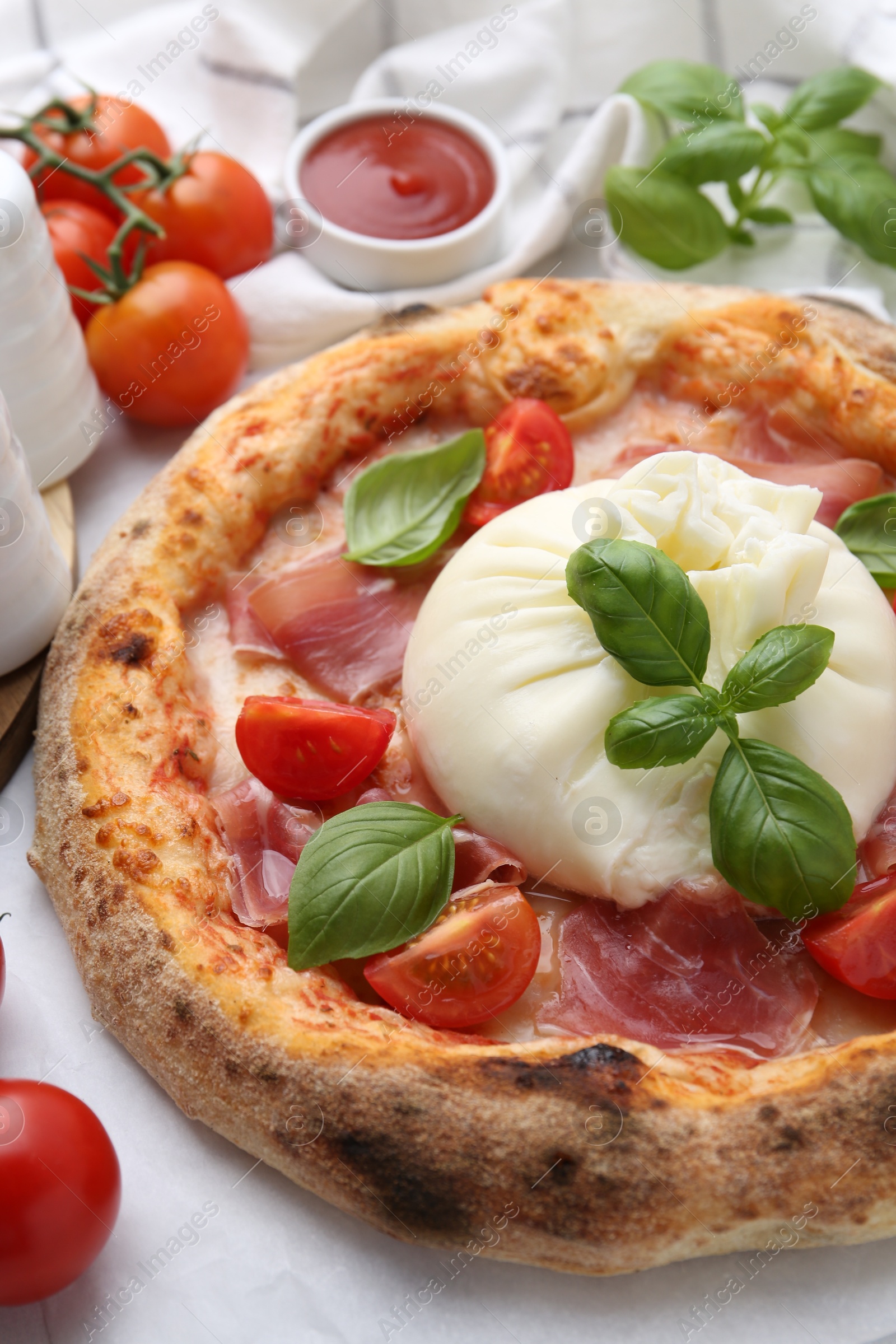 Photo of Delicious pizza with burrata cheese, basil, tomatoes and ham on table, closeup