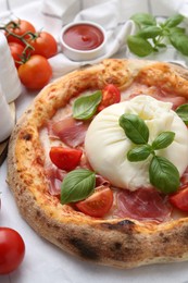 Photo of Delicious pizza with burrata cheese, basil, tomatoes and ham on table, closeup