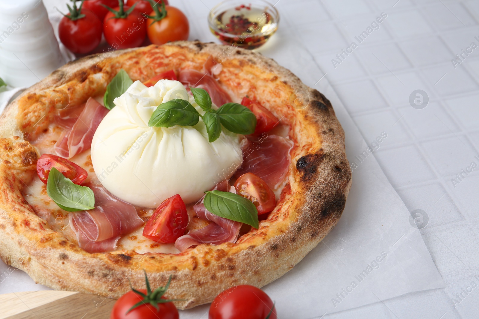 Photo of Delicious pizza with burrata cheese, basil, tomatoes and ham on white tiled table, closeup