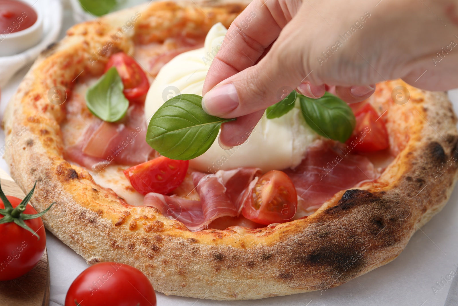 Photo of Woman adding basil to burrata pizza at table, closeup