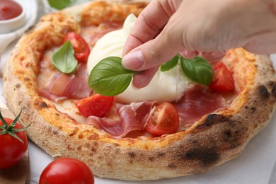 Photo of Woman adding basil to burrata pizza at table, closeup