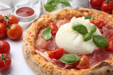 Photo of Delicious pizza with burrata cheese, basil, tomatoes and ham on table, closeup