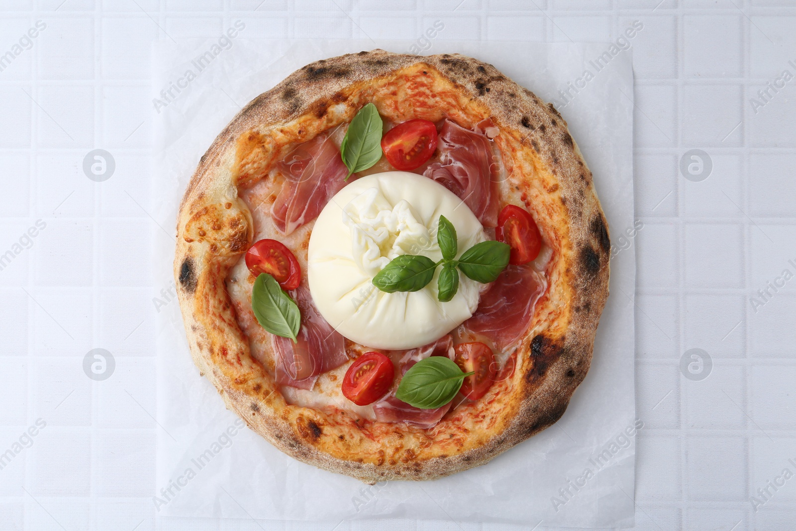 Photo of Delicious pizza with burrata cheese, basil, tomato and ham on white tiled table, top view