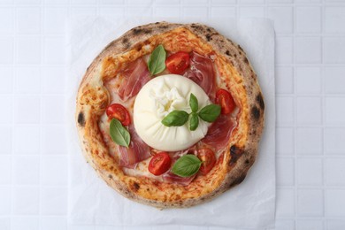 Delicious pizza with burrata cheese, basil, tomato and ham on white tiled table, top view