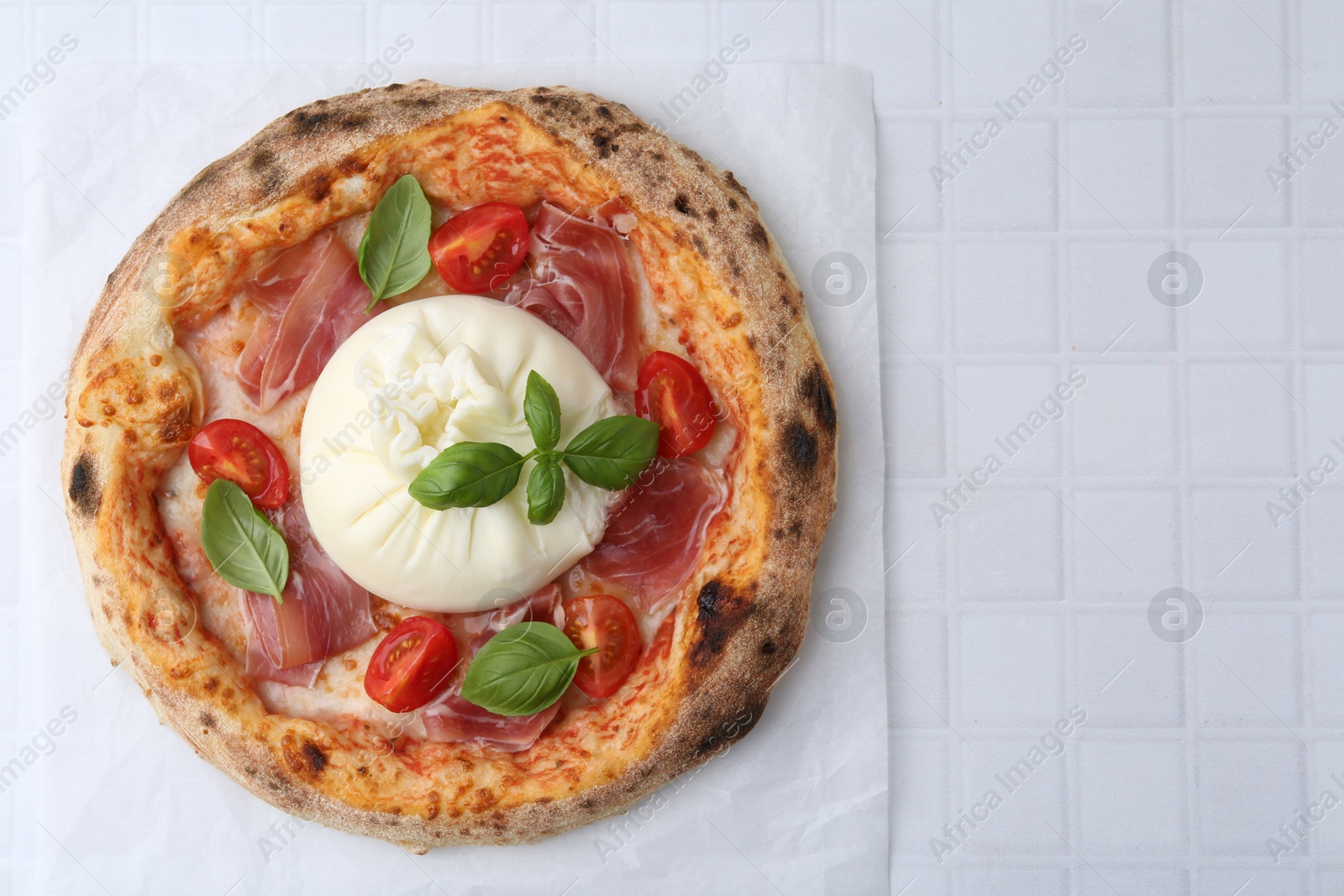 Photo of Delicious pizza with burrata cheese, basil, tomato and ham on white tiled table, top view. Space for text