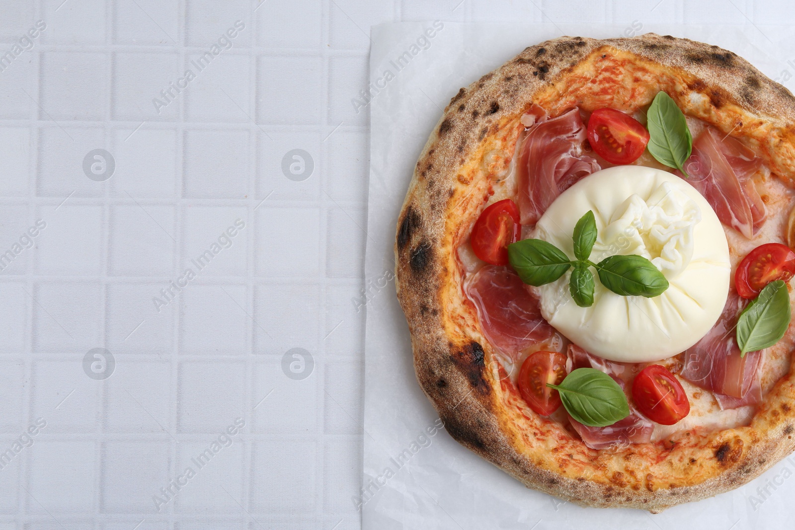 Photo of Delicious pizza with burrata cheese, basil, tomato and ham on white tiled table, top view. Space for text