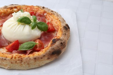 Photo of Delicious pizza with burrata cheese, basil, tomato and ham on white tiled table, closeup. Space for text