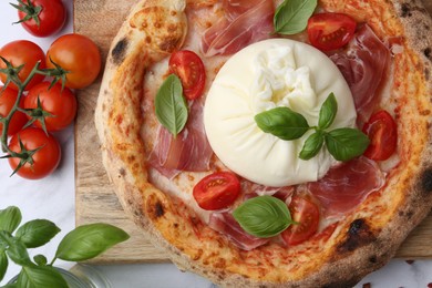 Photo of Delicious pizza with burrata cheese, basil, tomatoes and ham on white marble table, top view