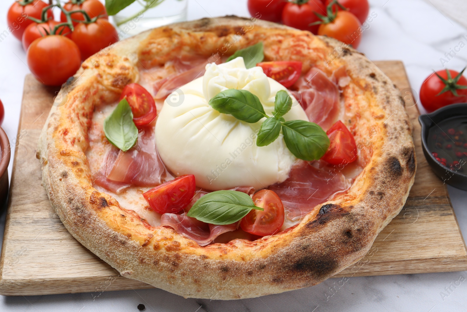 Photo of Delicious pizza with burrata cheese, basil, tomatoes and ham on table, closeup