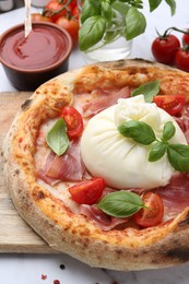 Photo of Delicious pizza with burrata cheese, basil, tomatoes and ham on table, closeup