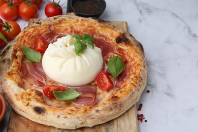 Photo of Delicious pizza with burrata cheese, basil, tomatoes and ham on white marble table, closeup