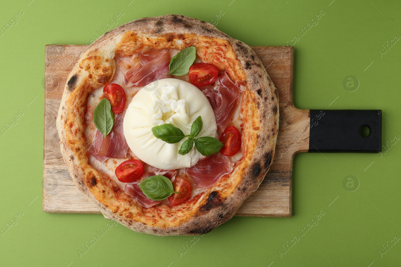 Photo of Delicious pizza with burrata cheese, basil, tomato and ham on green background, top view