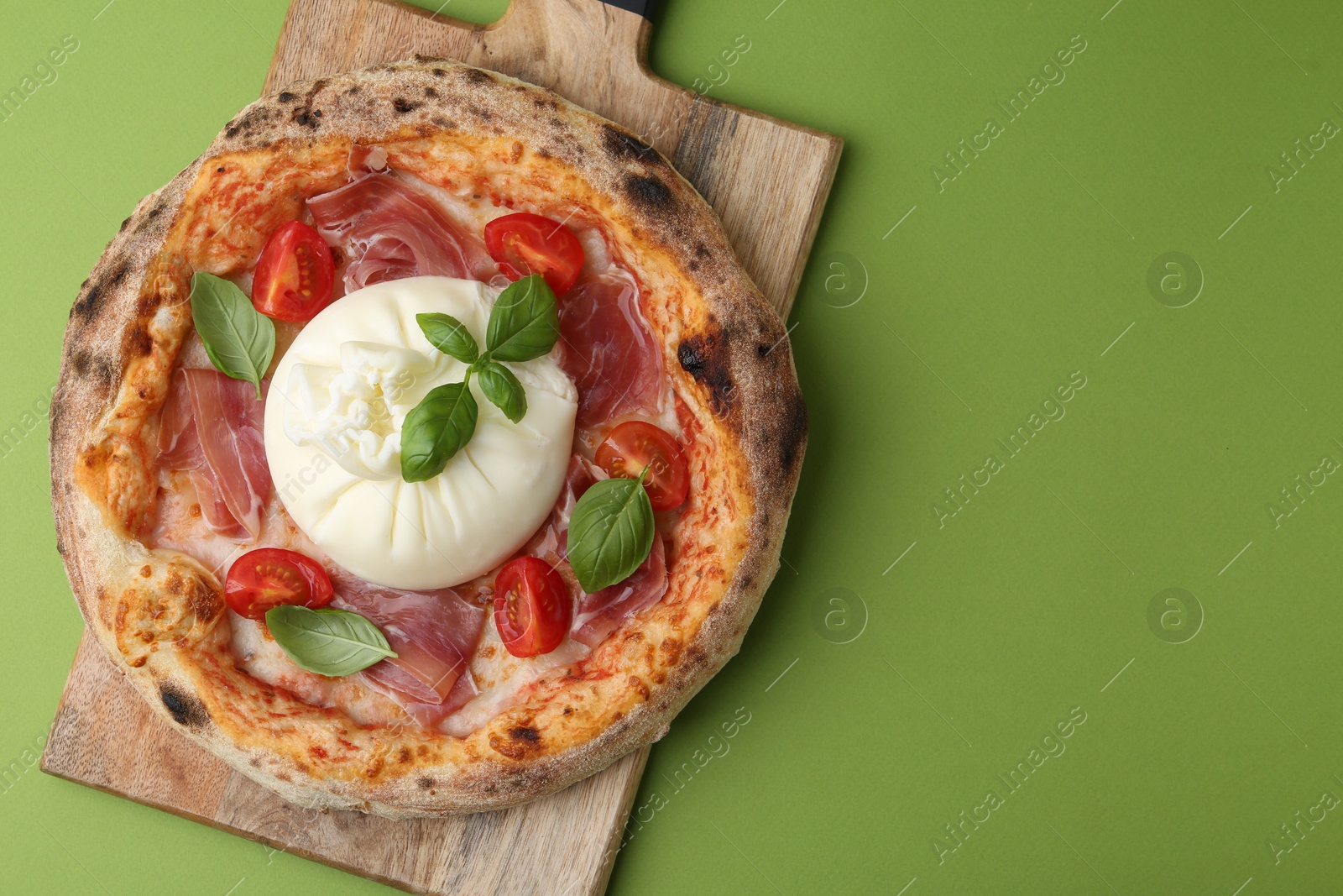 Photo of Delicious pizza with burrata cheese, basil, tomato and ham on green background, top view. Space for text