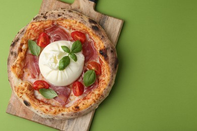 Photo of Delicious pizza with burrata cheese, basil, tomato and ham on green background, top view. Space for text