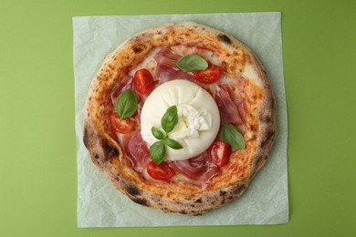 Photo of Delicious pizza with burrata cheese, basil, tomato and ham on green background, top view