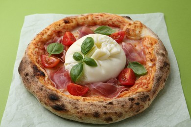 Photo of Delicious pizza with burrata cheese, basil, tomato and ham on green background, closeup