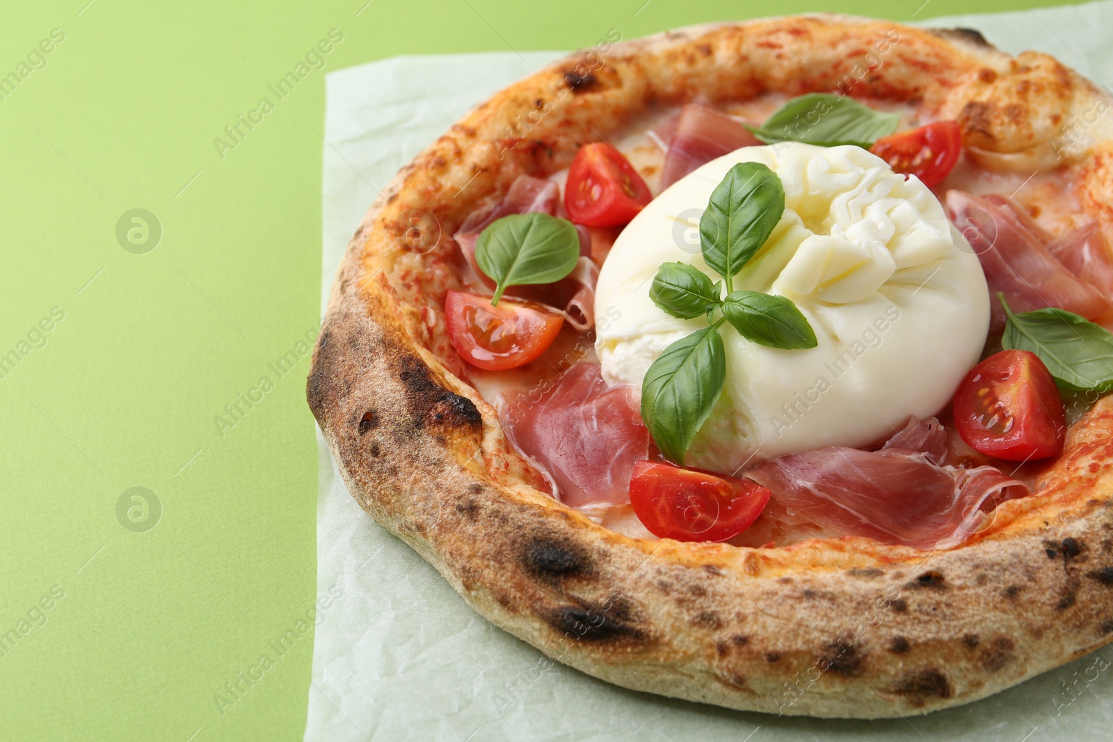 Photo of Delicious pizza with burrata cheese, basil, tomato and ham on green background, closeup