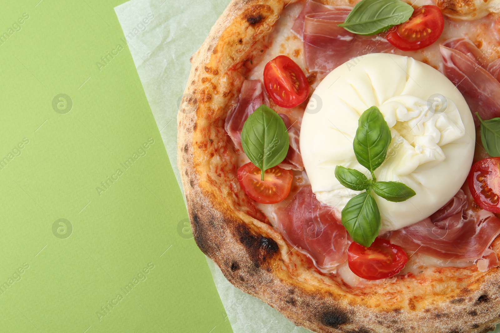 Photo of Delicious pizza with burrata cheese, basil, tomato and ham on green background, top view. Space for text