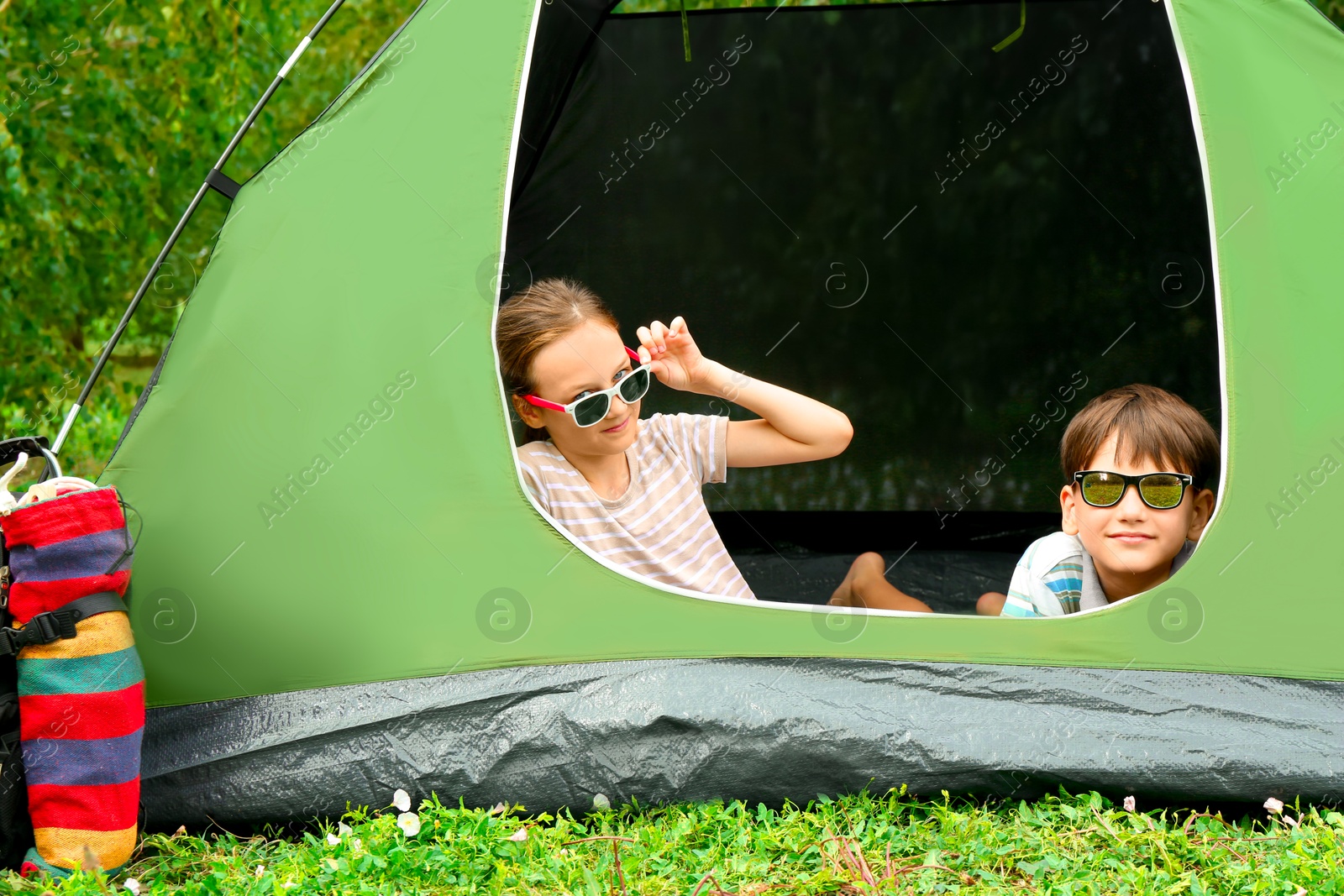 Photo of Girl and her brother resting in camping tent on green grass outdoors