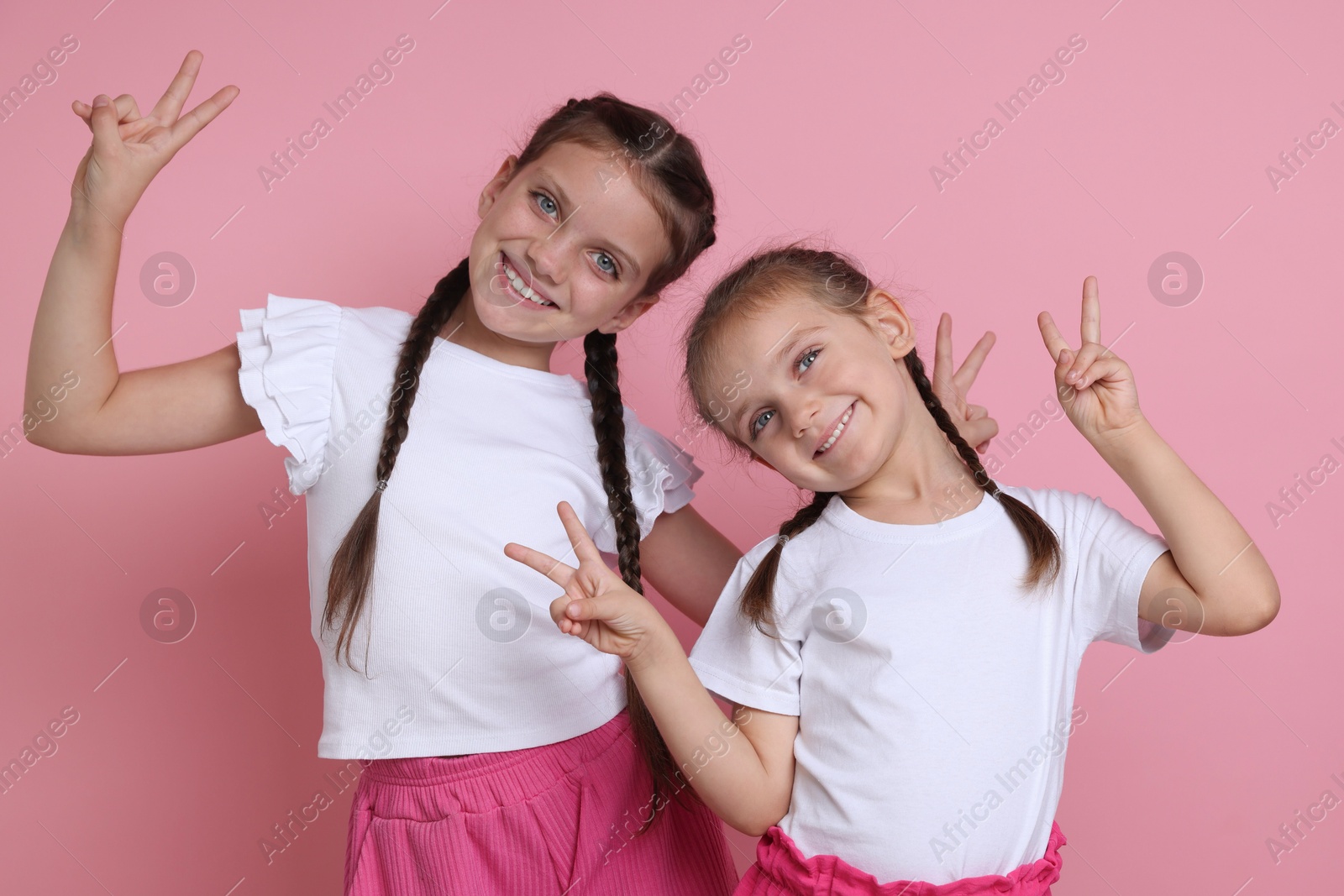 Photo of Portrait of cute little sisters on pink background