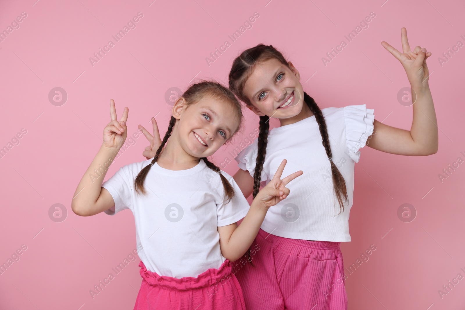 Photo of Portrait of cute little sisters on pink background