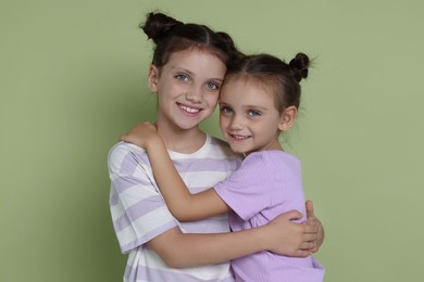 Portrait of cute little sisters on light green background