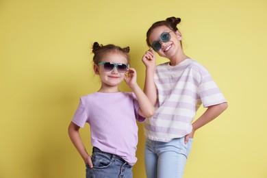 Portrait of cute little sisters on yellow background