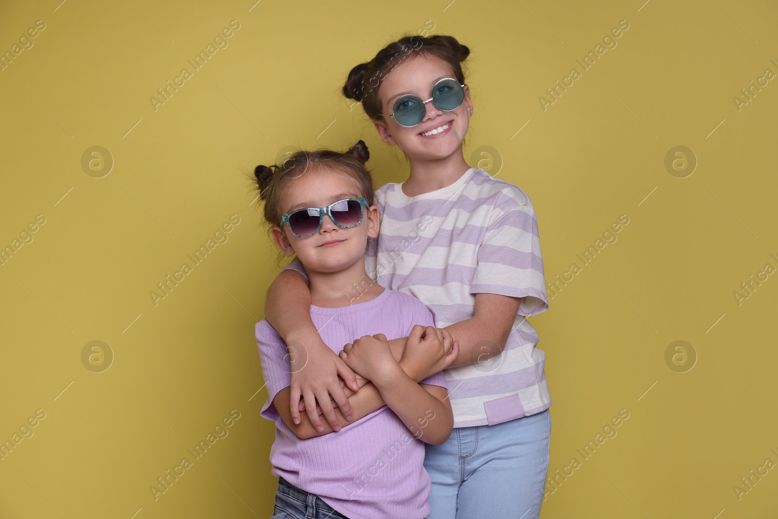 Photo of Portrait of cute little sisters on yellow background