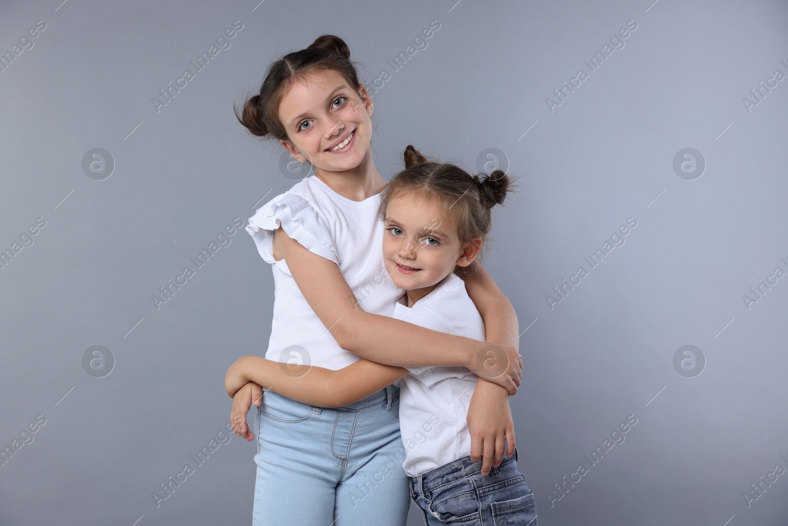 Photo of Portrait of cute little sisters on grey background