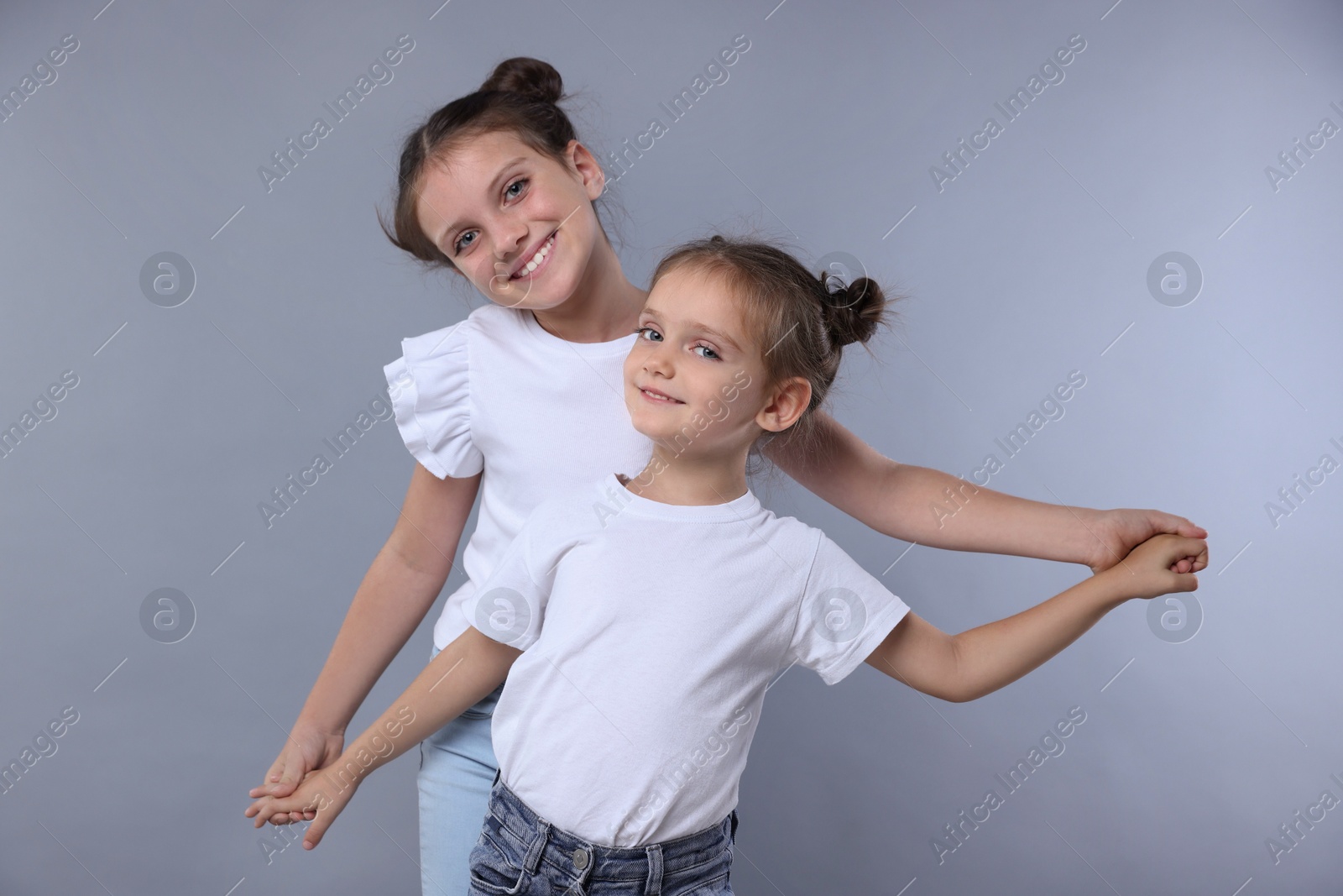 Photo of Portrait of cute little sisters on grey background