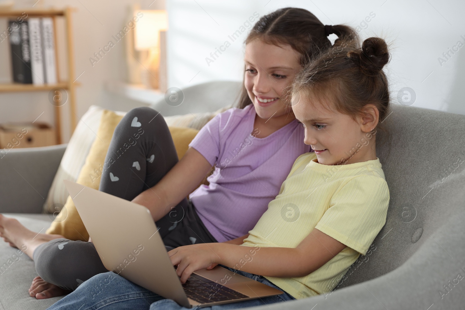 Photo of Cute little sisters with laptop spending time together at home