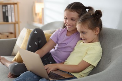 Photo of Cute little sisters with laptop spending time together at home