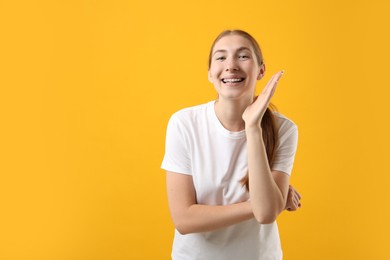 Photo of Smiling girl with braces on orange background, space for text