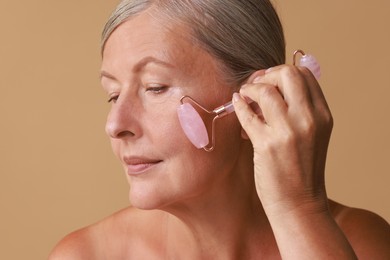 Photo of Beautiful woman doing facial massage with roller on beige background, closeup