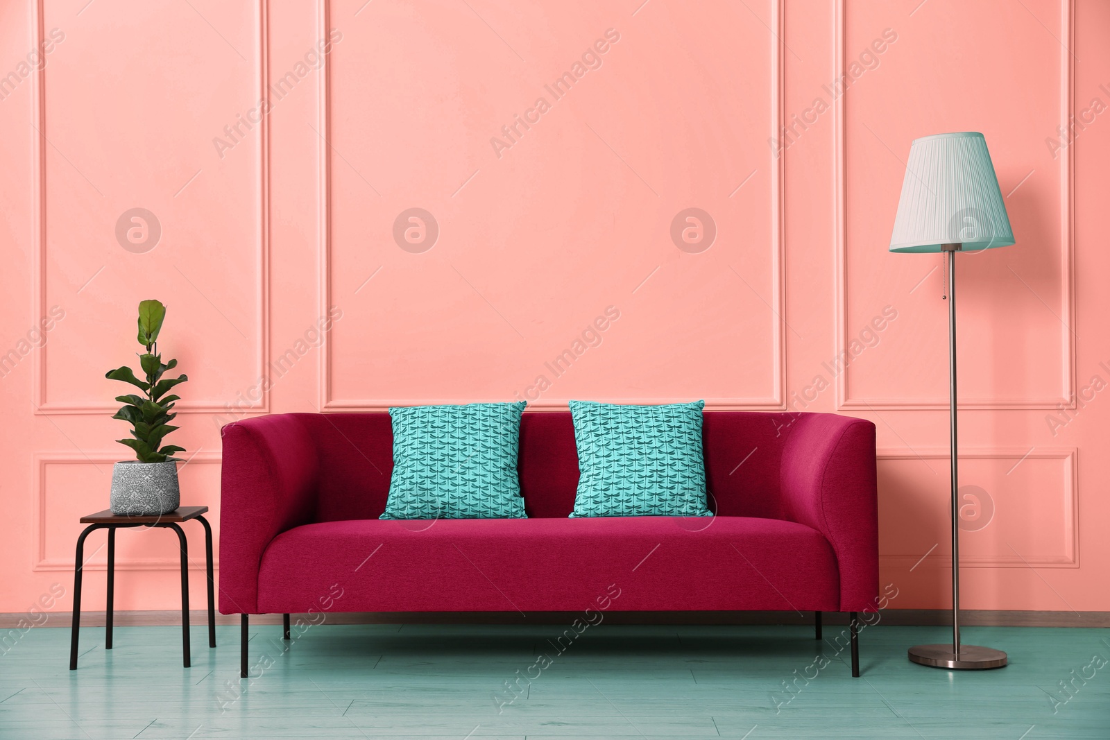 Image of Stylish sofa with cushions, floor lamp and side table with plant near wall