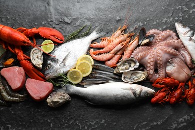 Fresh raw octopus, lobster, fish and other sea food on black table, top view