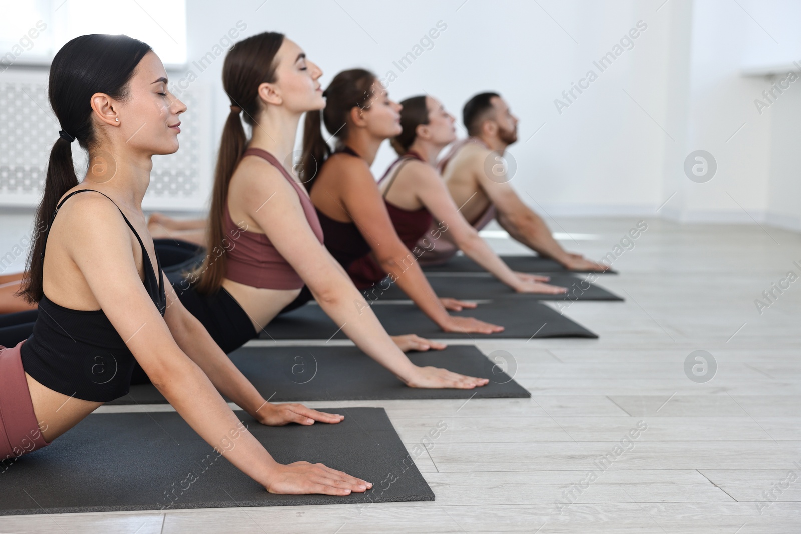 Photo of Group of people practicing yoga on mats in class. Space for text