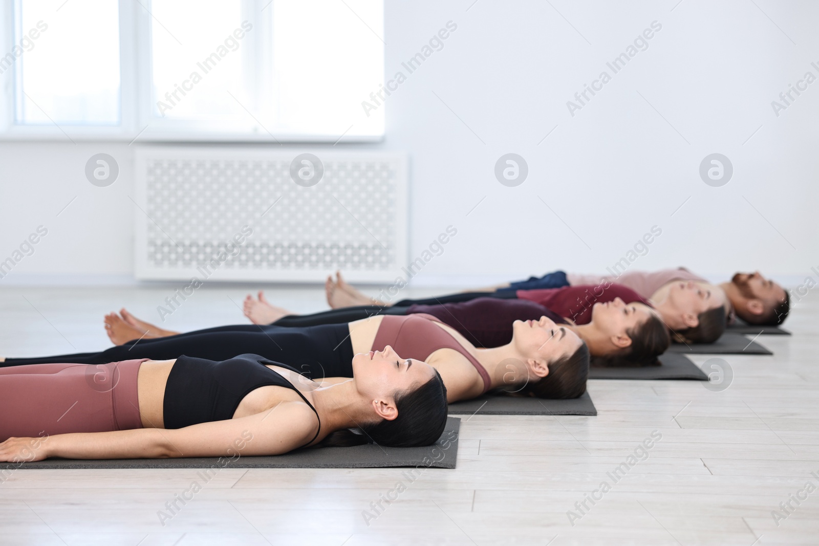 Photo of Group of people meditating on mats in yoga class. Space for text