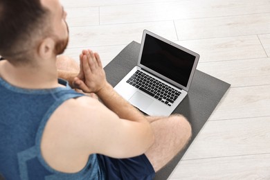 Photo of Man meditating near laptop on yoga mat at home