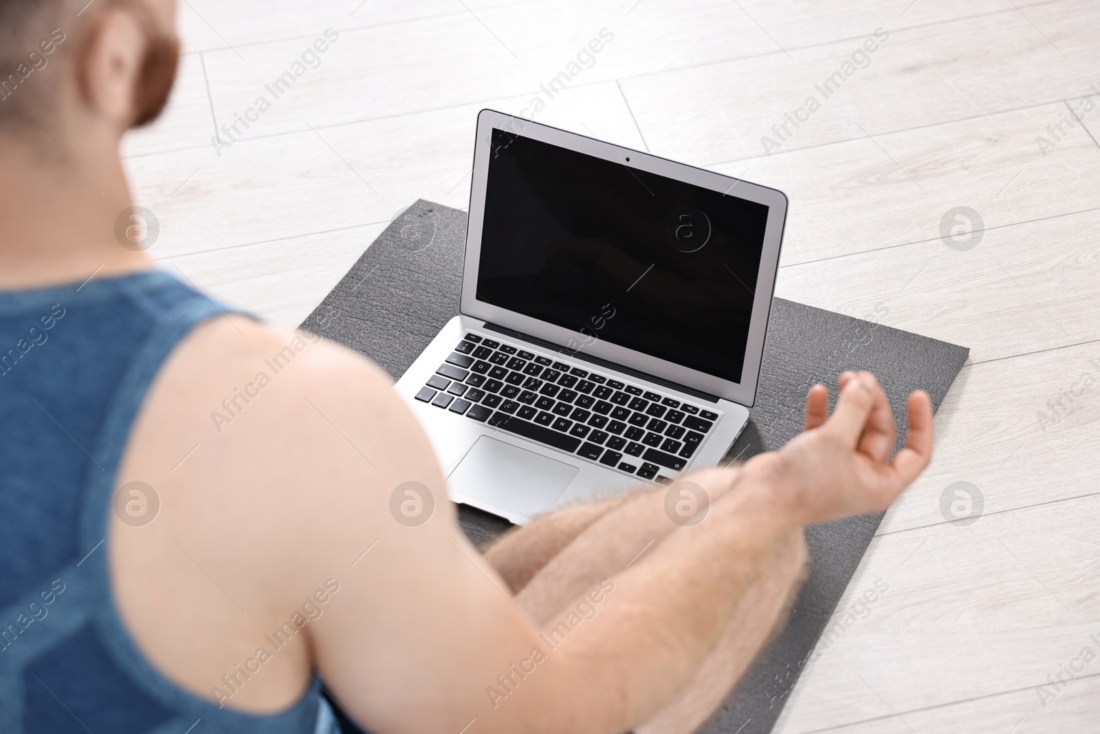 Photo of Man meditating near laptop on yoga mat at home, closeup