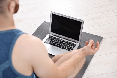 Photo of Man meditating near laptop on yoga mat at home, closeup