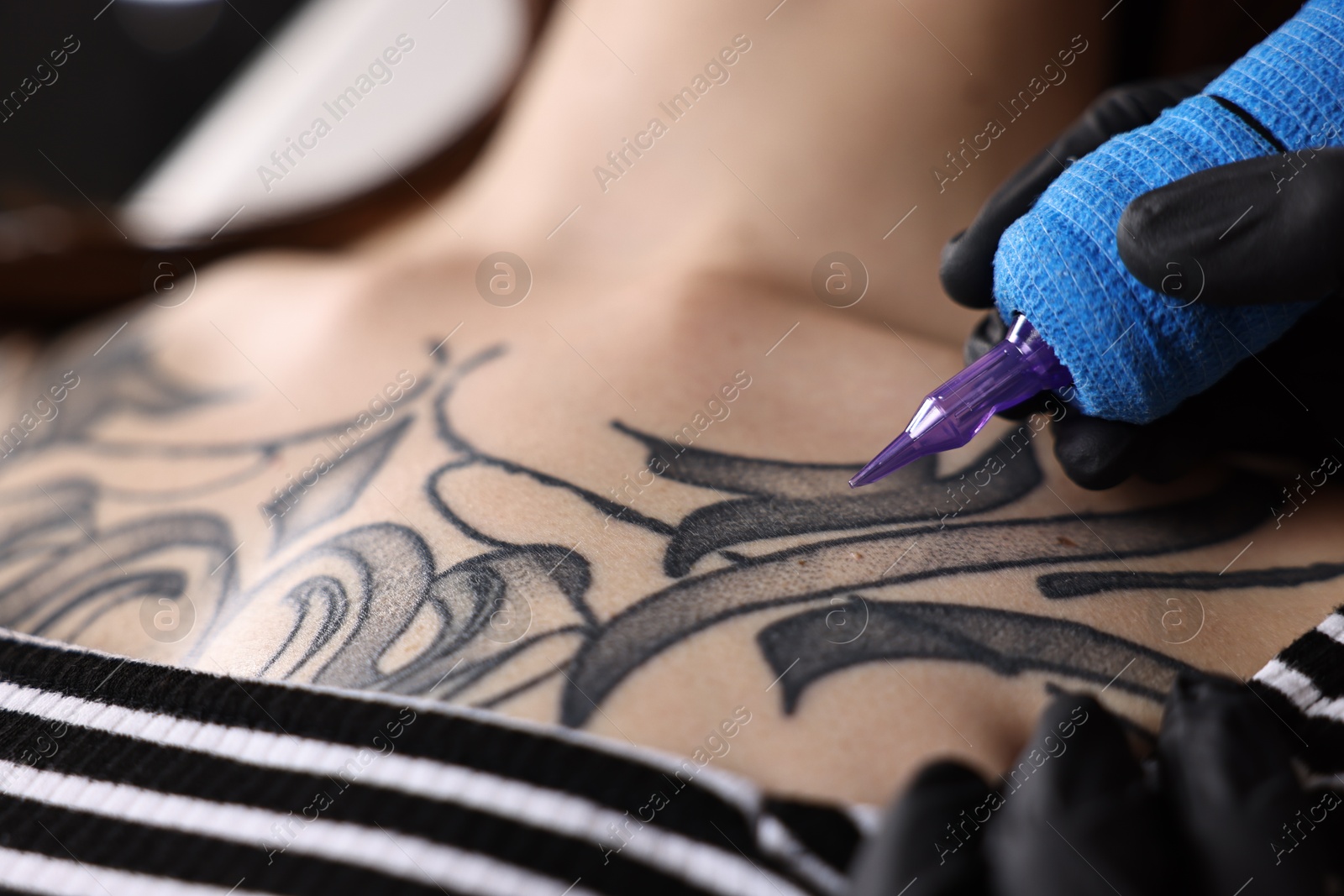 Photo of Professional artist tattooing woman with machine in salon, closeup