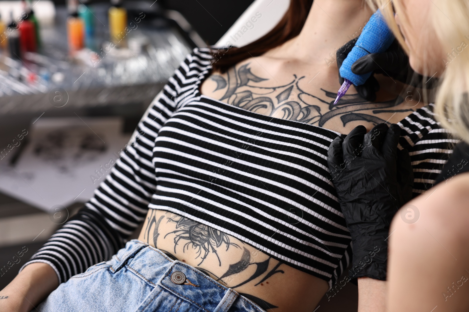 Photo of Professional artist tattooing woman with machine in salon, closeup