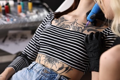 Professional artist tattooing woman with machine in salon, closeup