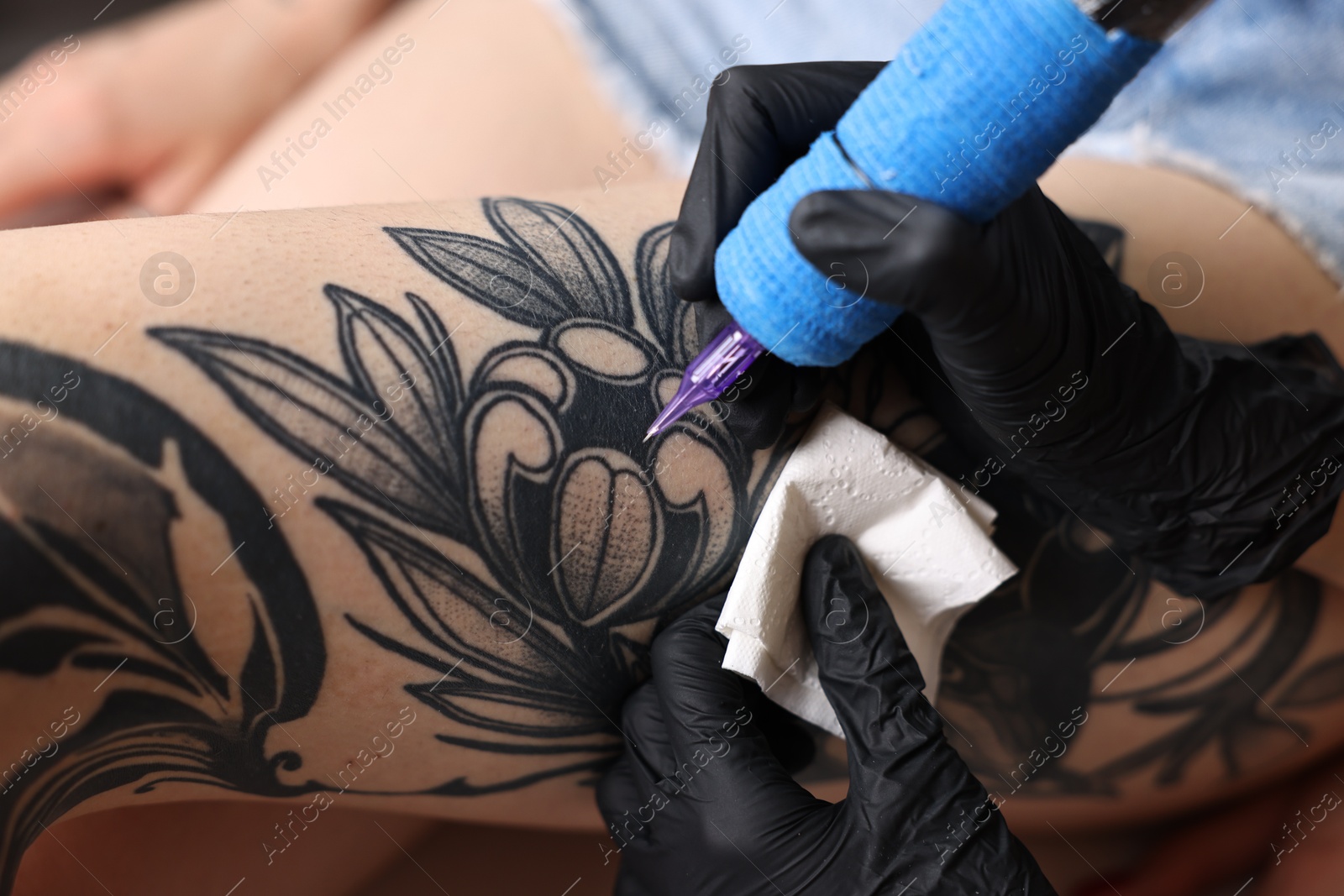 Photo of Professional artist tattooing woman's leg with machine in salon, closeup