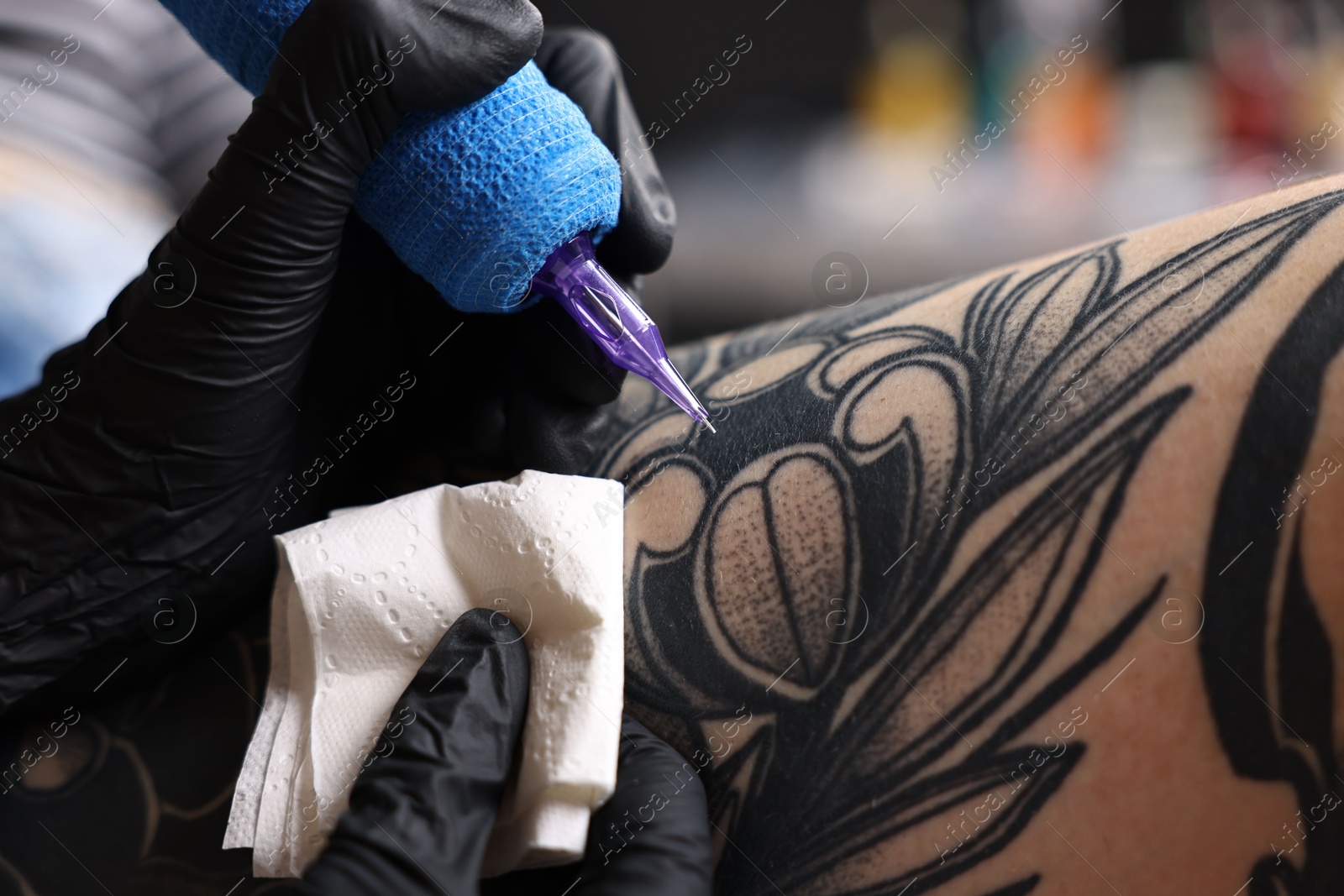 Photo of Professional artist tattooing woman's leg with machine in salon, closeup