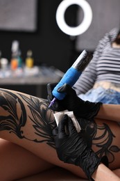 Photo of Professional artist tattooing woman's leg with machine in salon, closeup