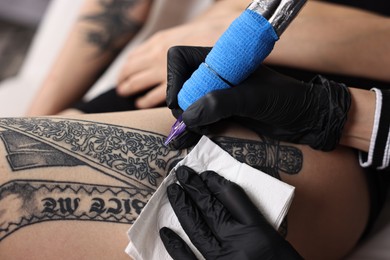 Photo of Professional artist tattooing woman's leg with machine in salon, closeup