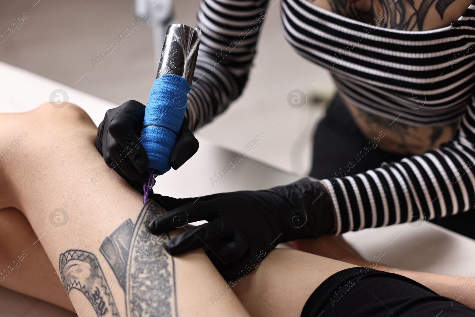 Photo of Professional artist tattooing woman's leg with machine in salon, closeup